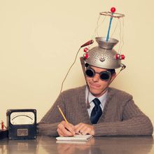 Conceptual retro image of a man wearing a silly mind reading gadget on his head, holding a pencil, and writing his thoughts down in a notebook.