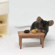 A mouse stands behind a toy table with two pieces of food on it.