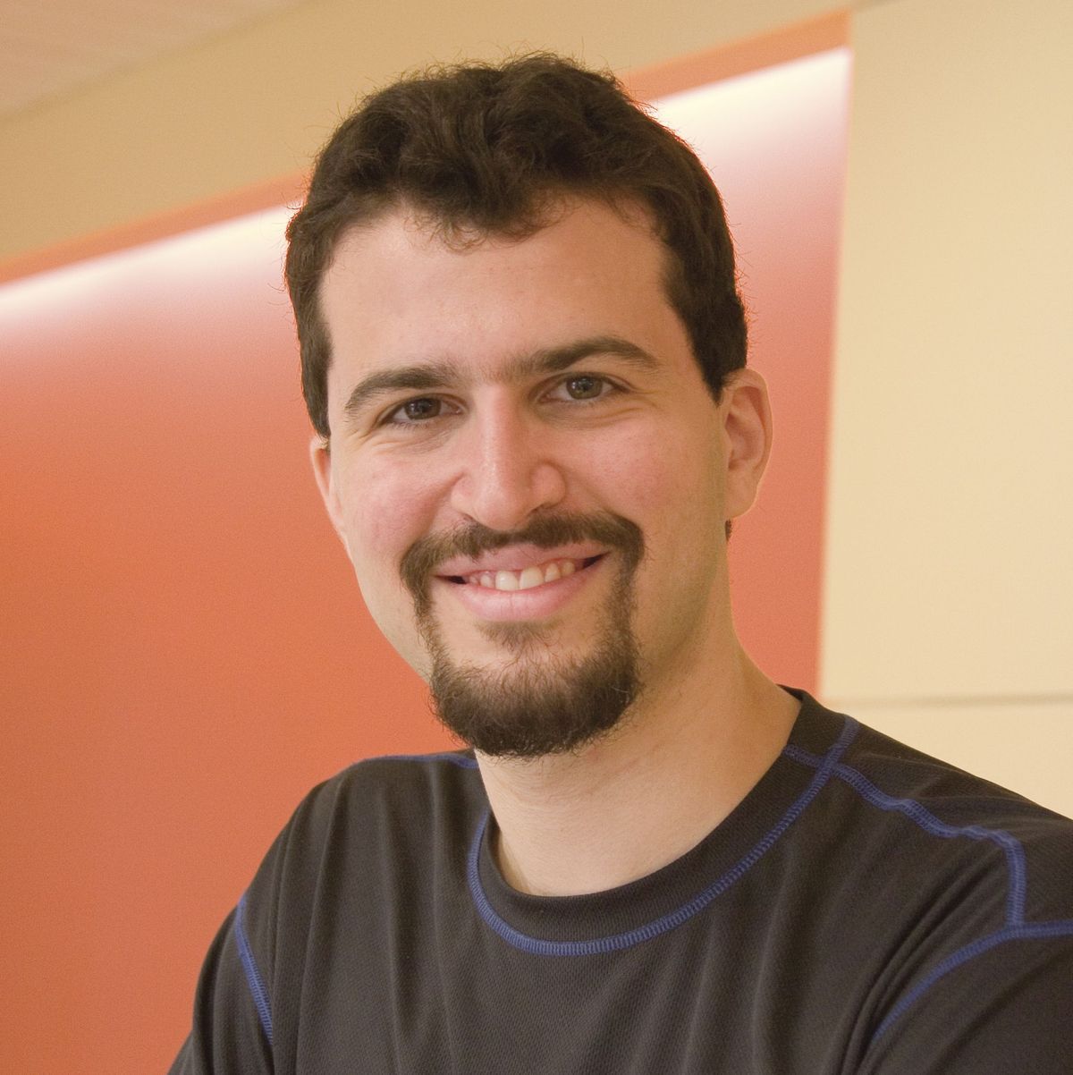 Image of Erez Lieberman Aiden, a molecular geneticist at Baylor College of Medicine, who is involved in researching 3D structure of genomes. He wears a black shirt and smiles at the camera.