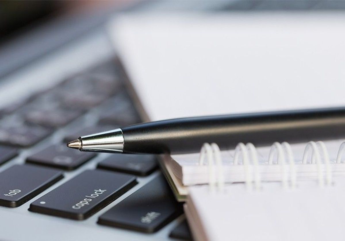 A ballpoint pen placed on top of a notebook that is sitting on top of a laptop keyboard.