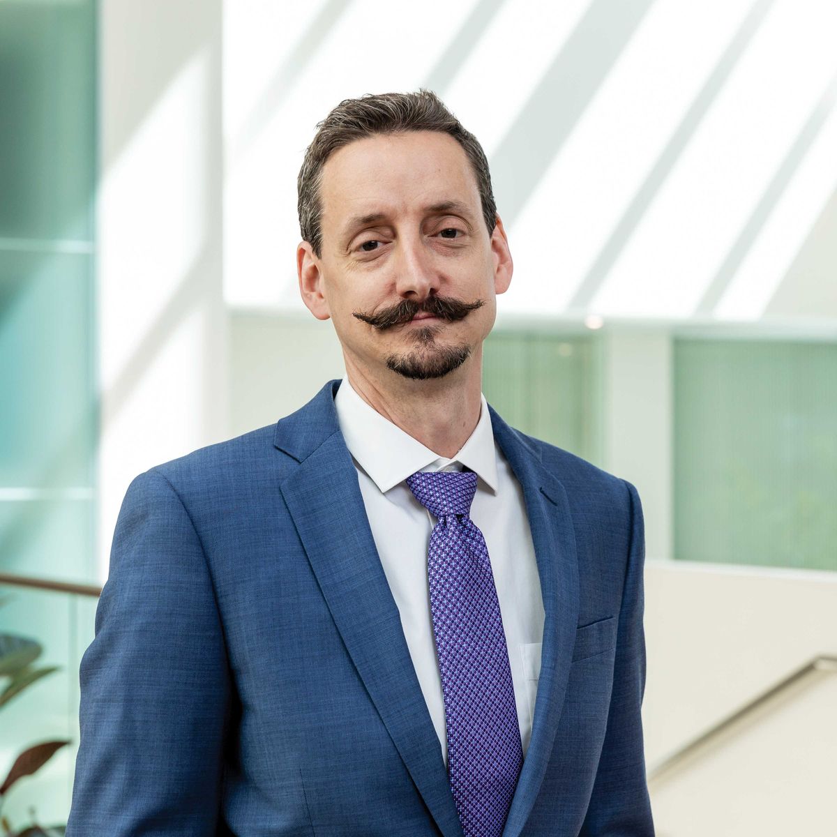 Ian Wickersham wears a collared shirt and a blazer against a white background.