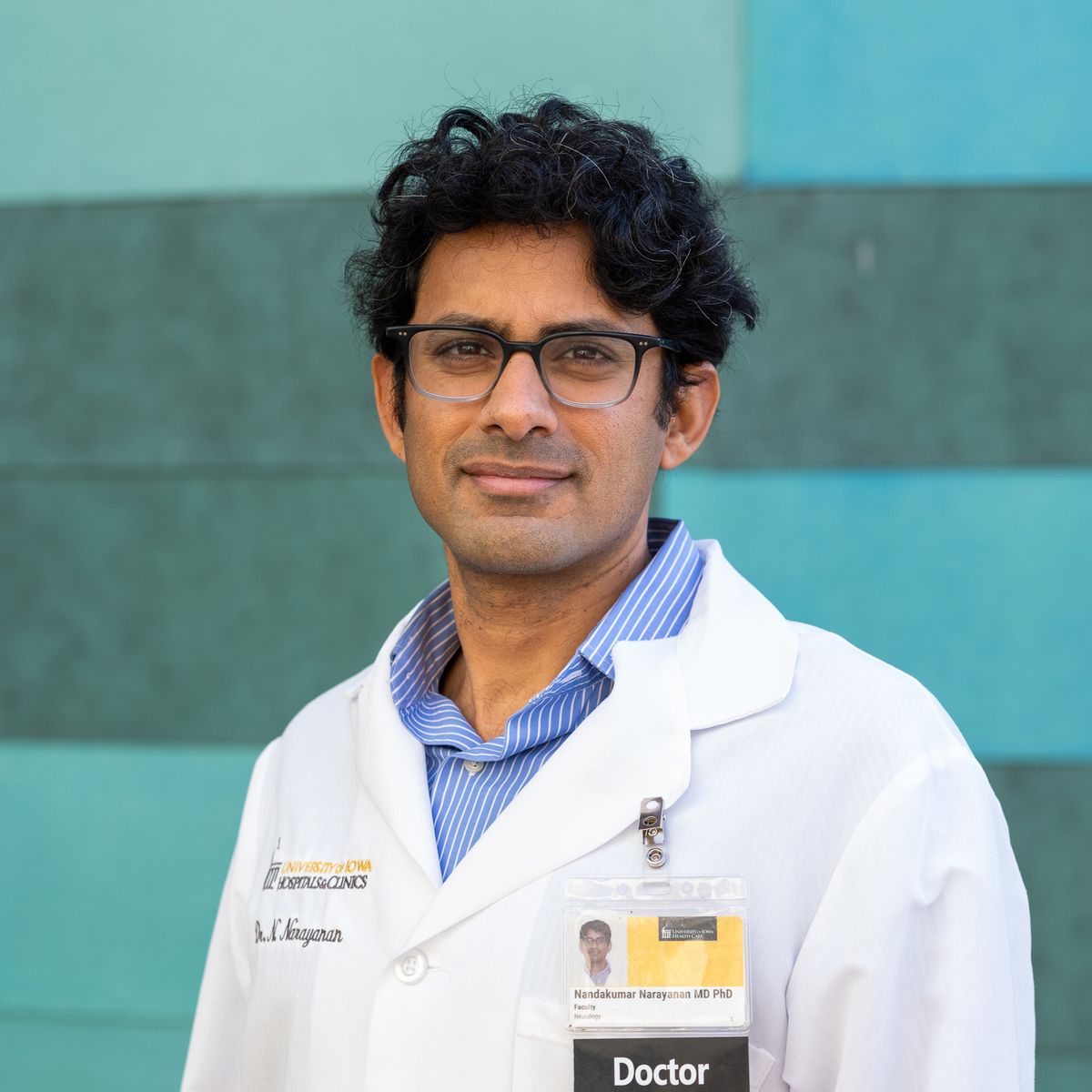 Nandakumar Narayanan wears a lab coat and stands in front of a blue background.