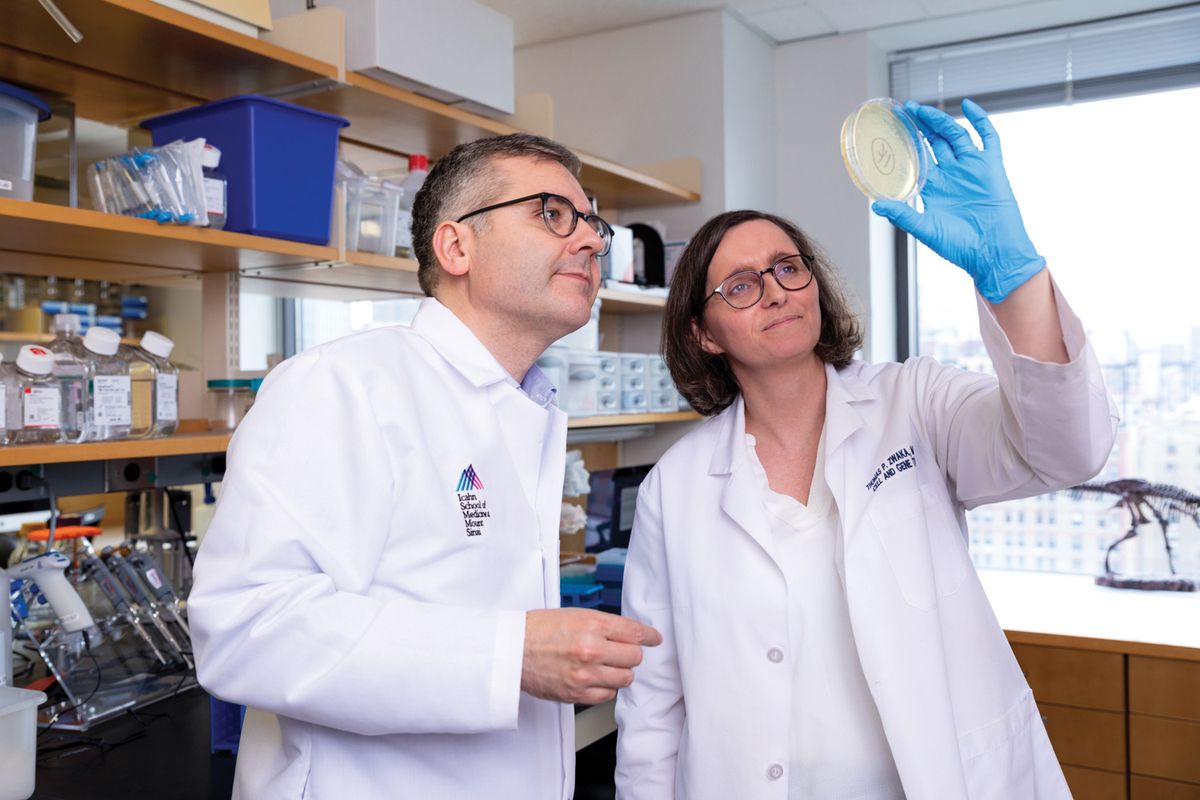 Thomas Zwaka and Marion Dejosez wear white lab coats and examine a petri dish.