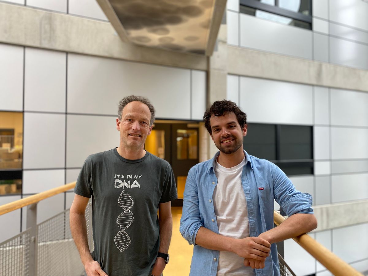 Two men stand side-by-side in a walk way for a photograph.