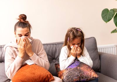 A woman and a child sitting on a couch blowing their noses.