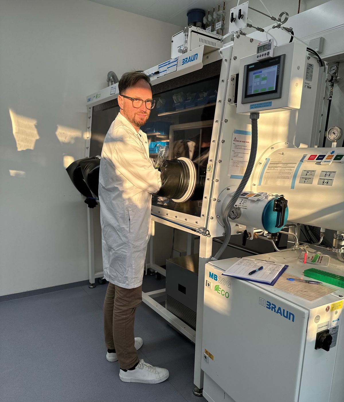 A man wear a laboratory coat. His hands are inside a safety laboratory hood.