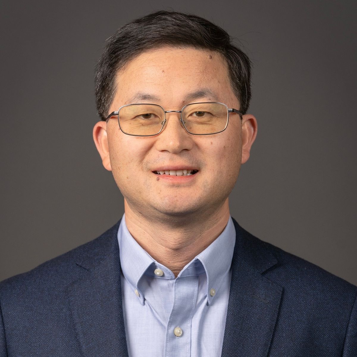 Headshot of bioengineer Liangfang Zhang. He smiles at the camera. He is wearing glasses and is wearing a light blue shirt under a dark blue jacket.