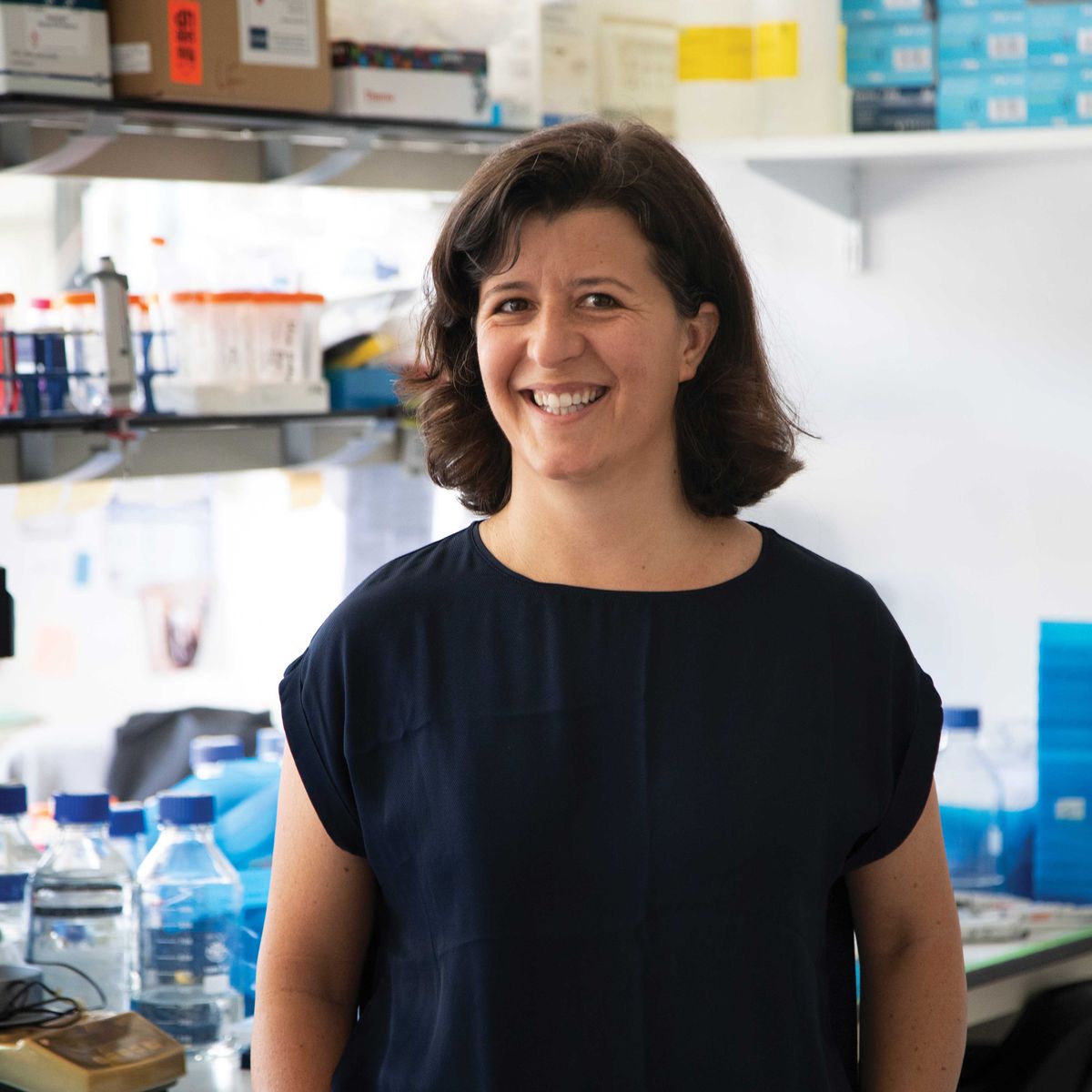 A woman is in a research laboratory. She wears a black shirt and smiles. 