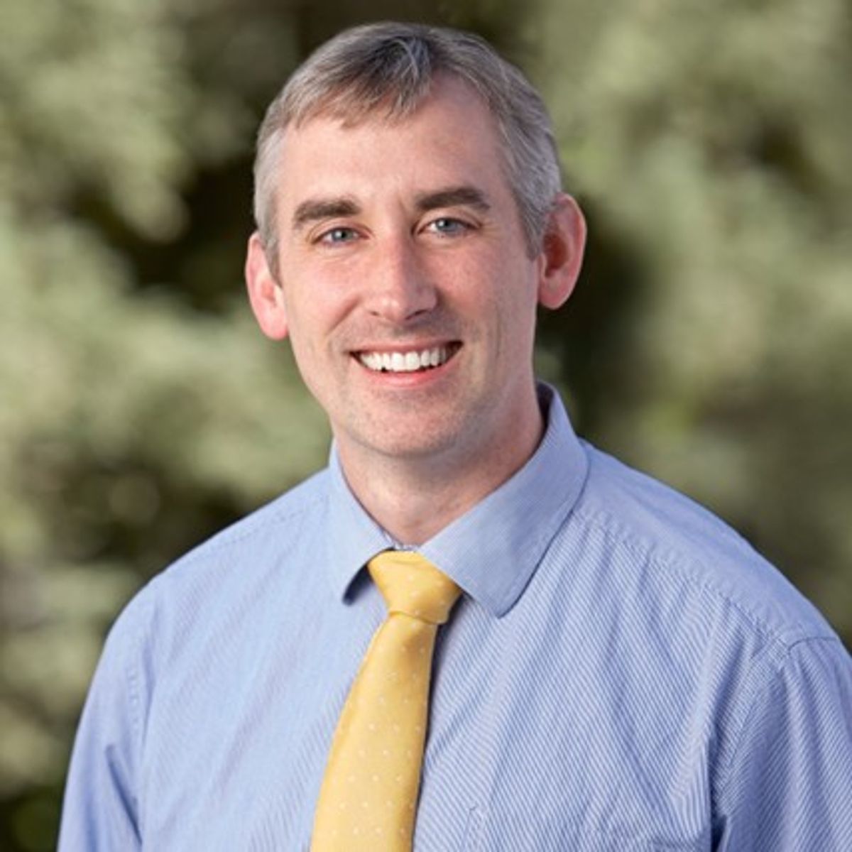 Headshot of Paul George, a physician scientist at Stanford University. He wears a blue shirt and yellow tie.