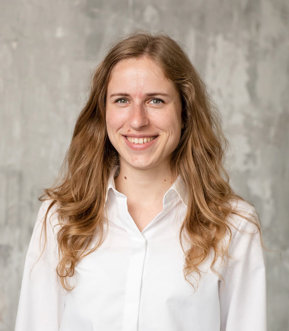 Sophie Farkas wears a white button-down and smiles against a grey backdrop.