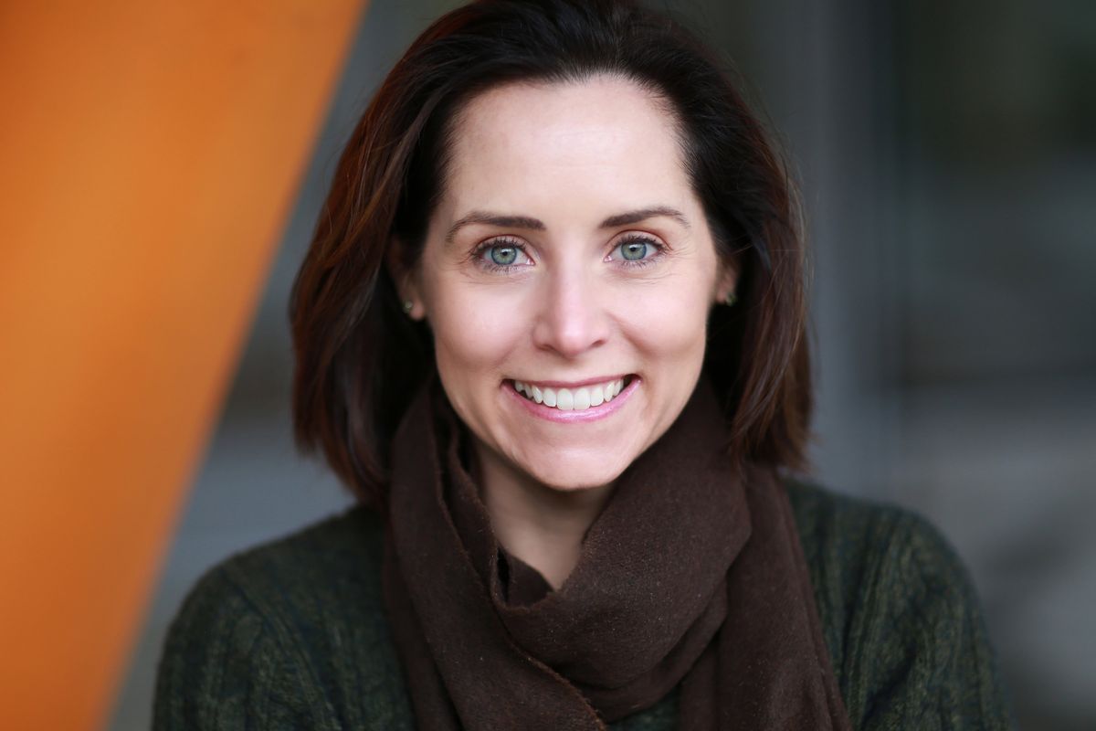 A young woman wears a dark green pullover and a winter scarf. She looks at the camera and smiles. 