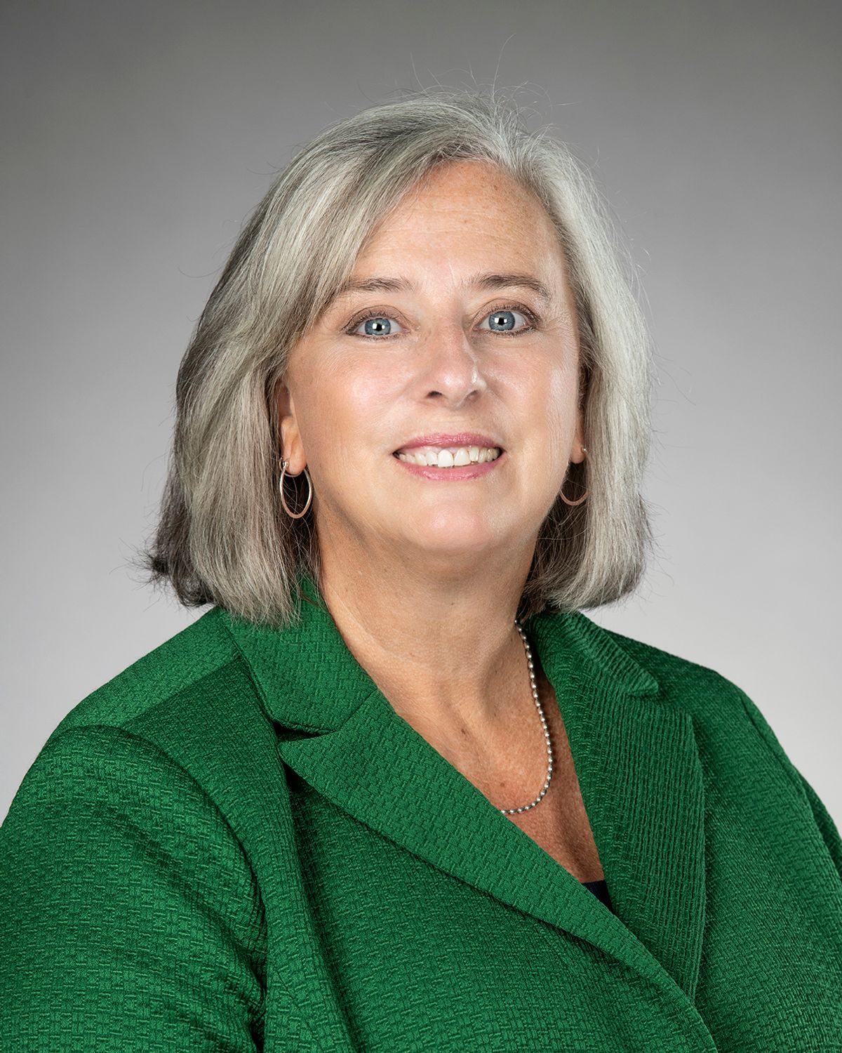 The photo shows a woman wearing a green blazer and smiling at the camera. 