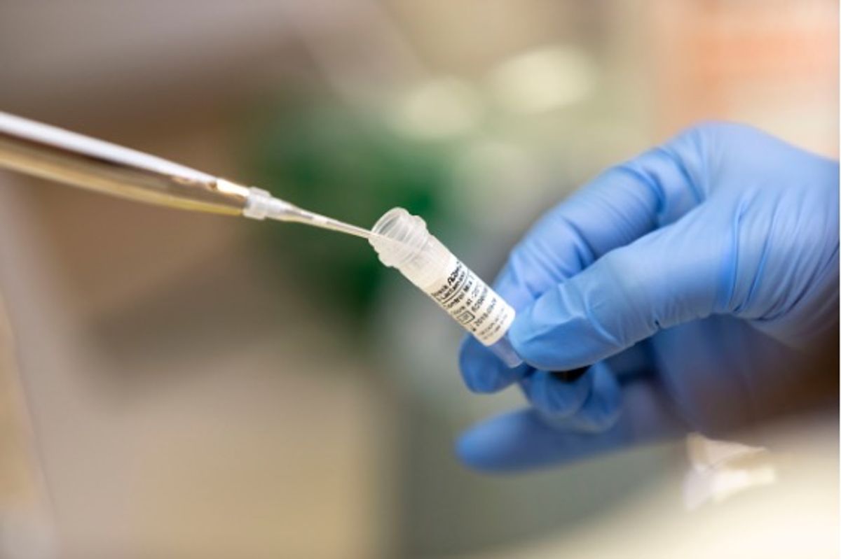 Conceptual image of a scientist pipetting liquid from a vial, showing a blue gloved hand on the right and a pipette tip on the left.