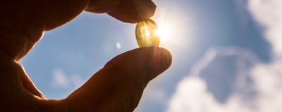 A hand holding a pill against sunlight.