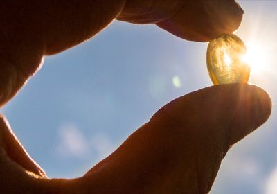 A hand holding a pill against sunlight.