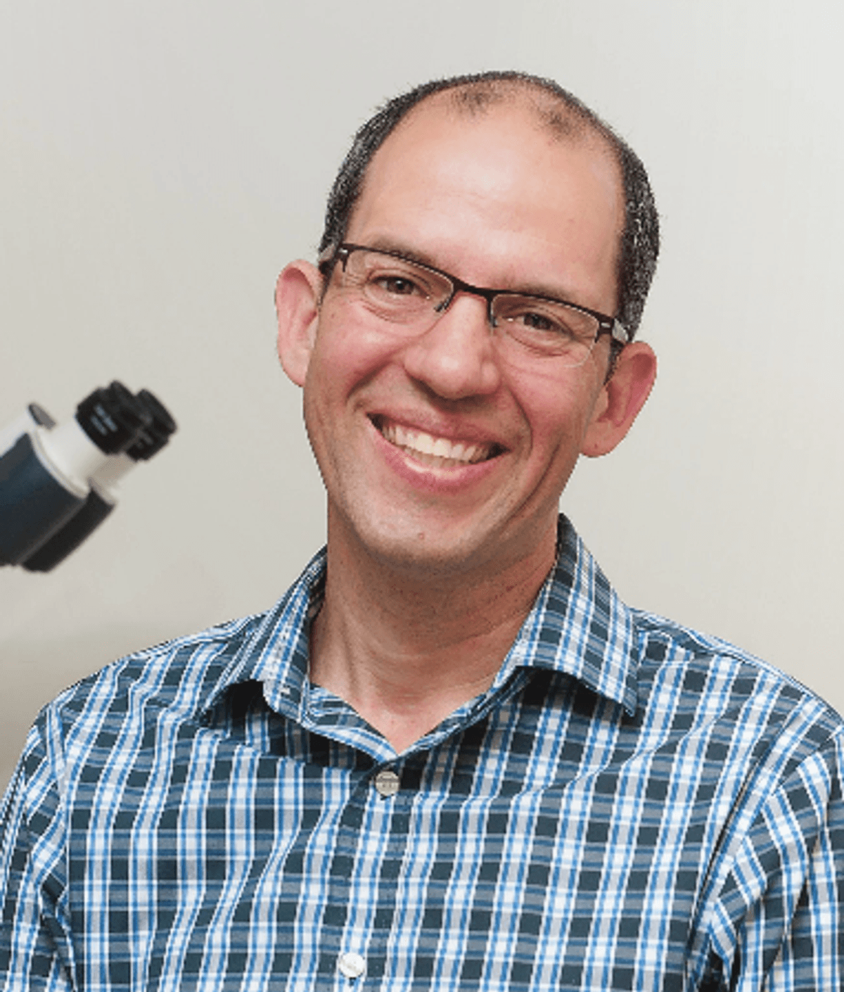 Eytan Wine wears a collared shirt and smiles in front of a microscope.