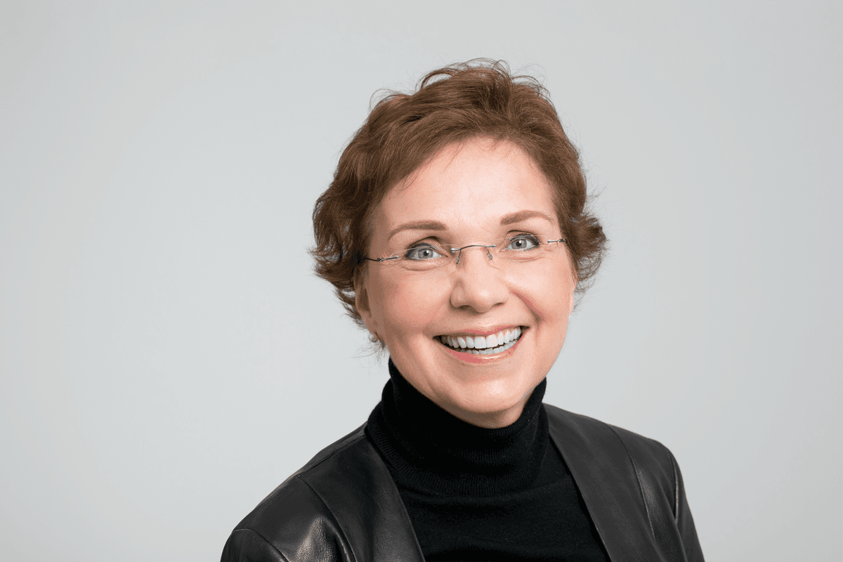 Petra Arck wears a black turtleneck and smiles against a white background.