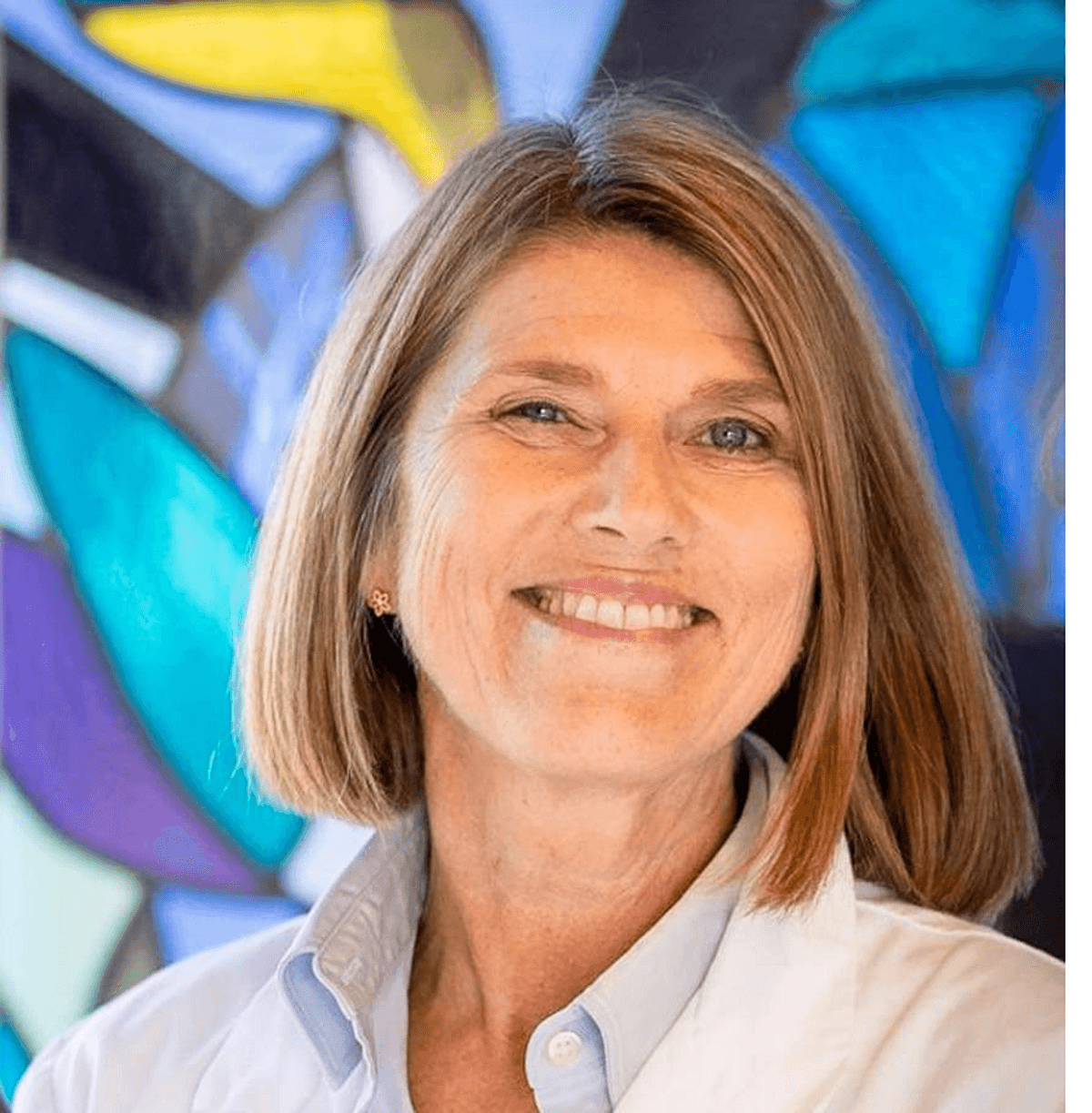 Anne Cathrine Staff wears a collared shirt and smiles against a multicolored background.